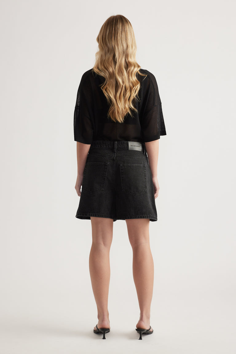 Back view of a woman in high-rise black A-line denim shorts, an oversized black tee and heeled sandals