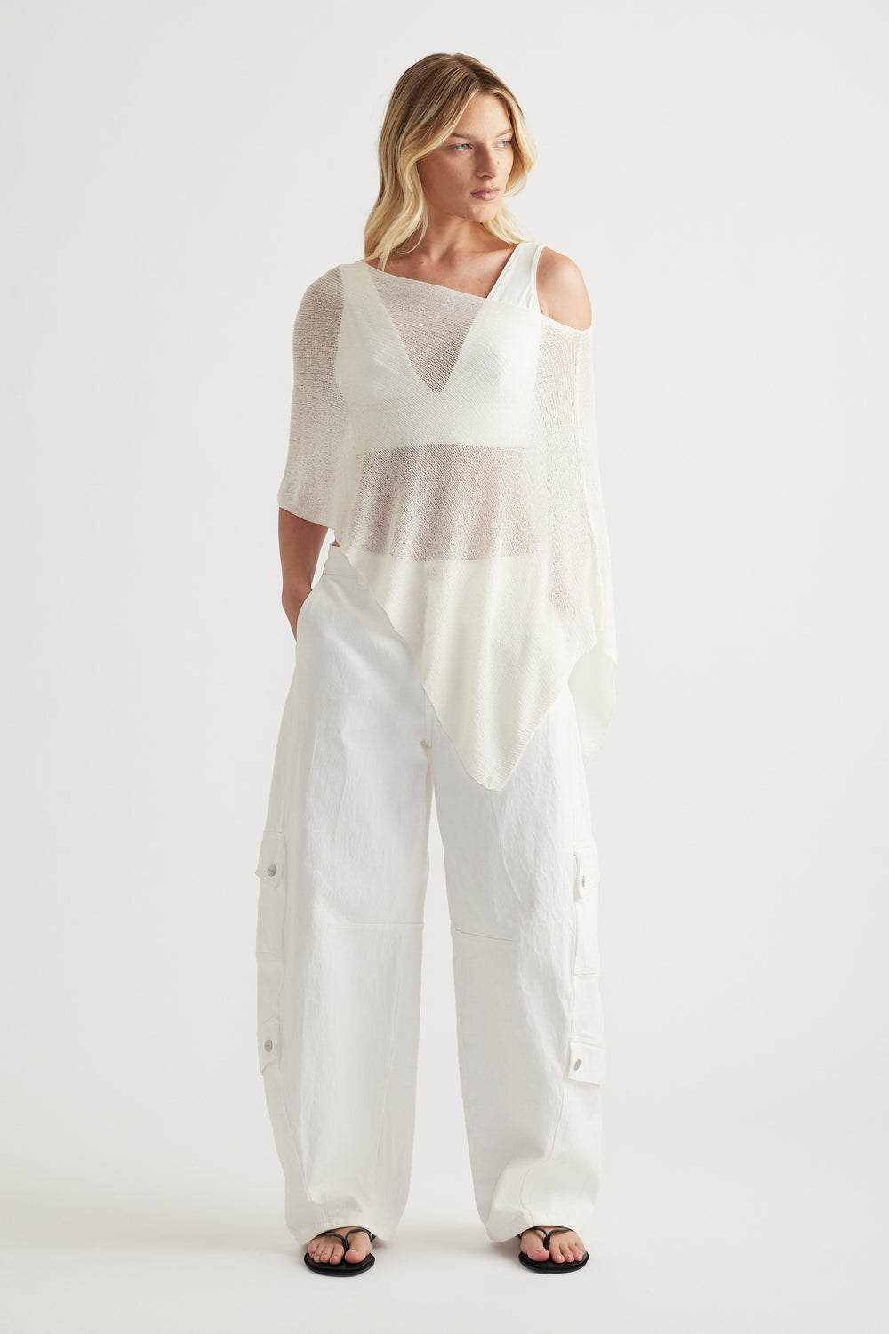 Woman in a lightweight white asymmetric knit poncho with a boat neckline and relaxed silhouette