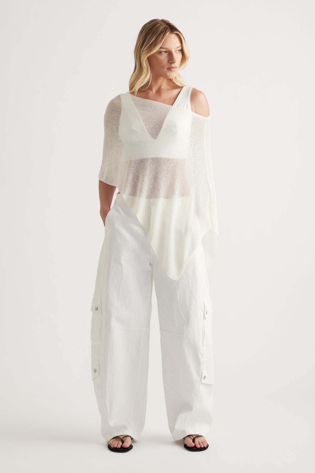 Woman in a lightweight white asymmetric knit poncho with a boat neckline and relaxed silhouette