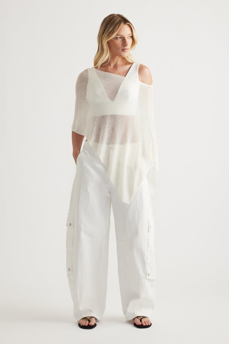 Woman in a lightweight white asymmetric knit poncho with a boat neckline and relaxed silhouette