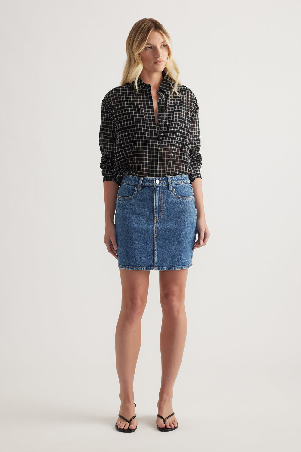 Woman wearing a high rise blue denim mini skirt with a black checked shirt and sandals