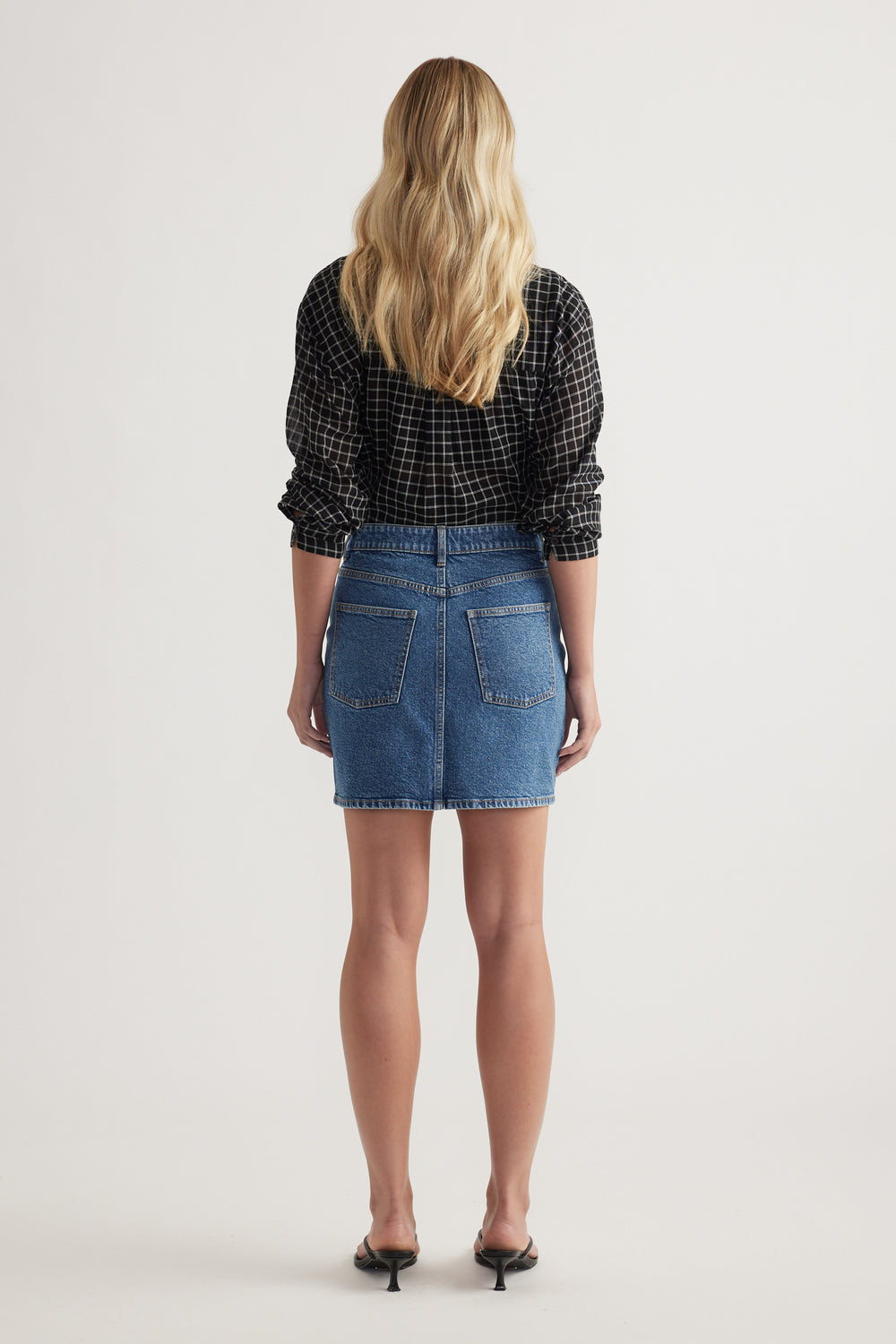 Back view of a woman wearing a high rise denim mini skirt with a black checked shirt