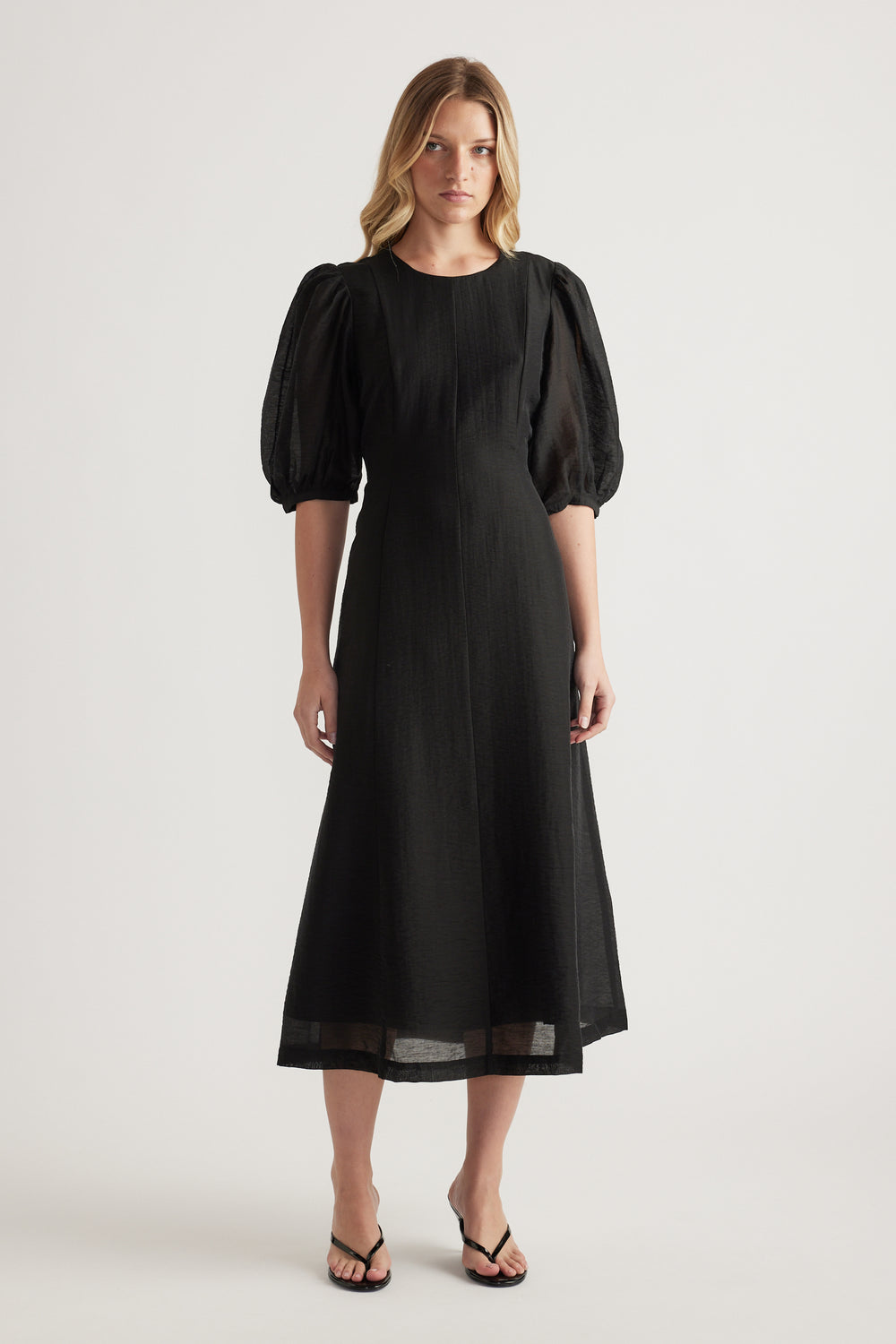 Woman wearing a black textured midi dress with puff sleeves and round neckline