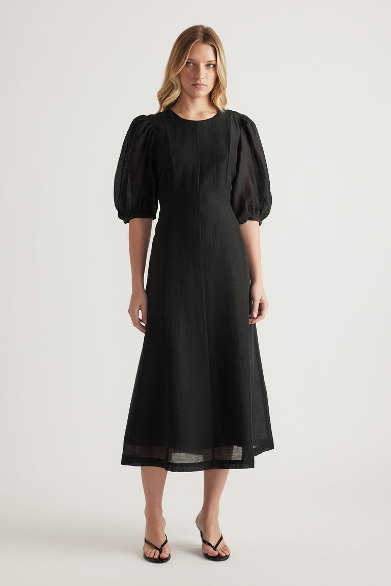 Woman wearing a black textured midi dress with puff sleeves and round neckline