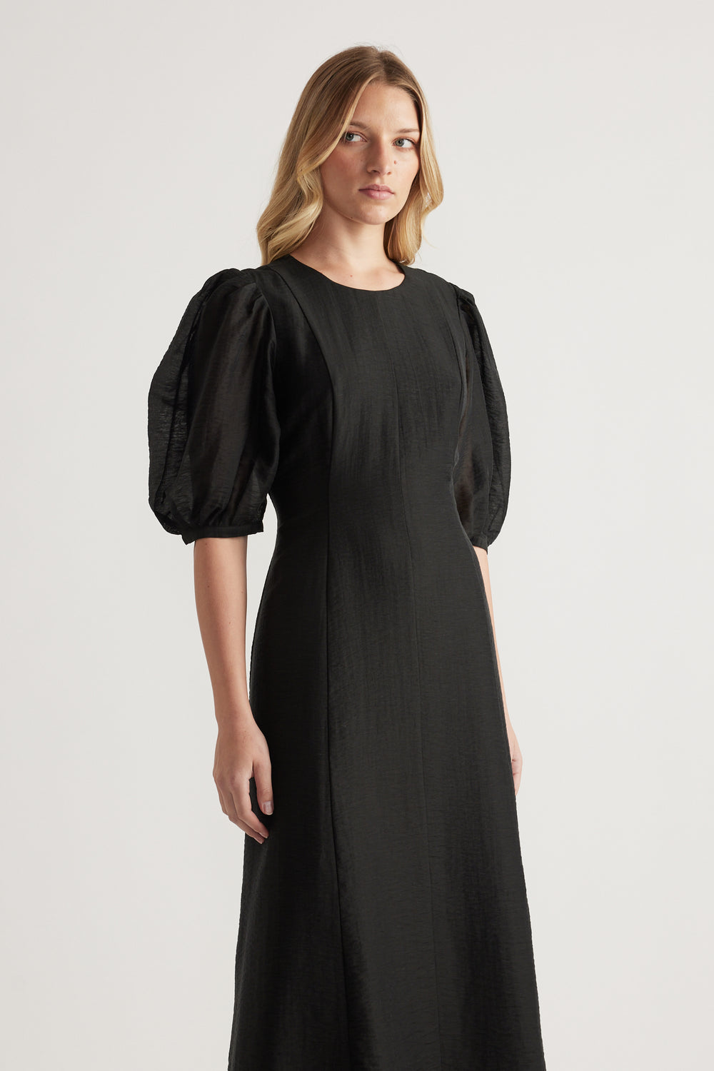 Model wearing a black textured midi dress with puff sleeves and a round neckline