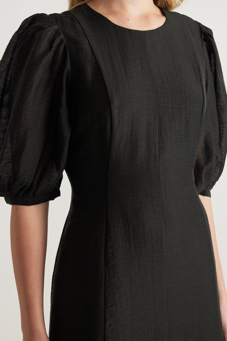 Woman wearing a black textured midi dress with puff sleeves and a round neckline