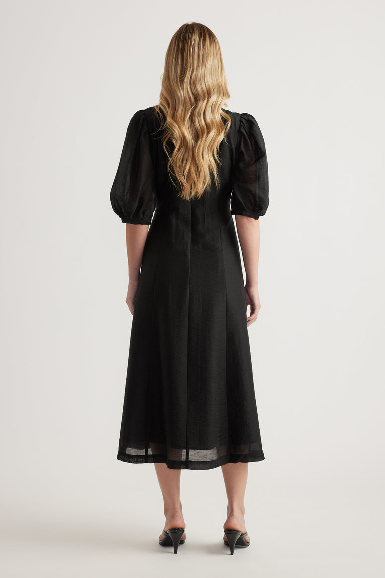 Woman wearing a black textured midi dress with puff sleeves, viewed from behind
