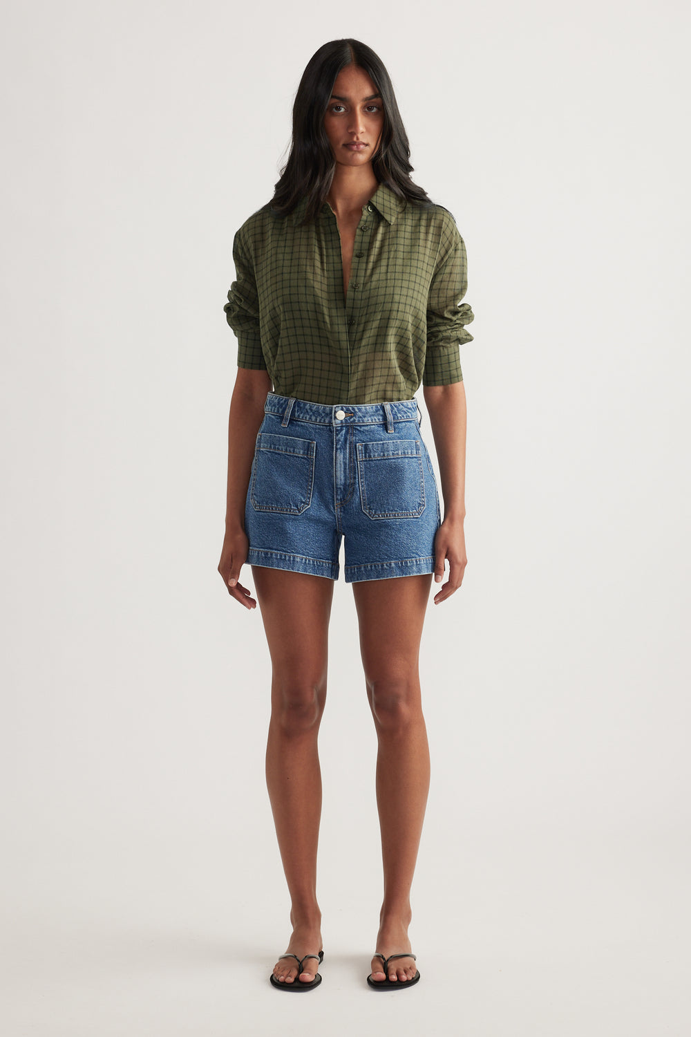 Model wearing high rise blue denim shorts with front patch pockets and an olive check shirt