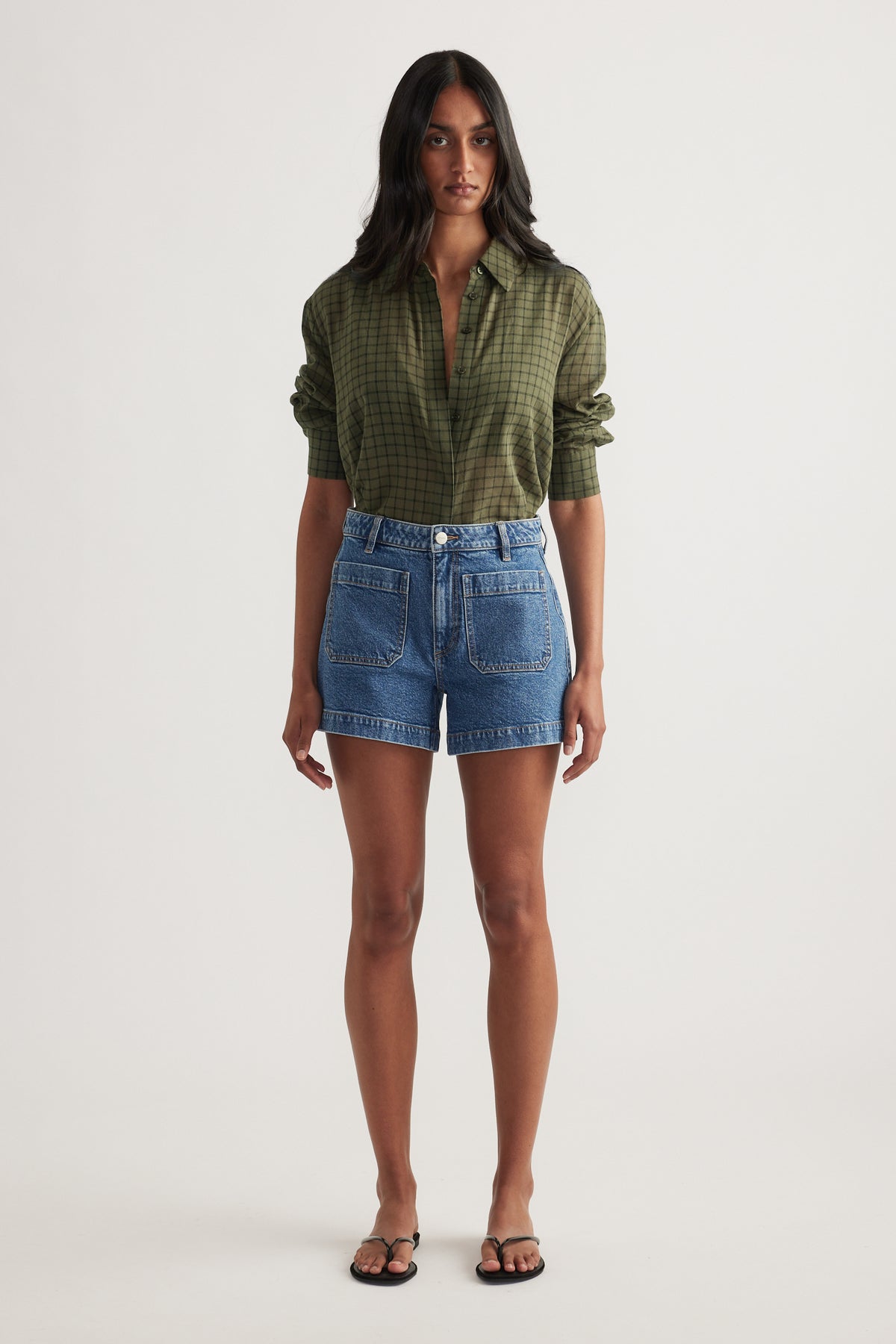 Model wearing high rise blue denim shorts with front patch pockets and an olive check shirt