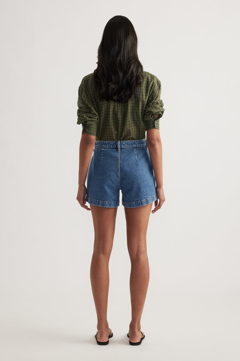 Back view of a woman wearing high rise blue denim shorts with rolled hems and a green plaid shirt