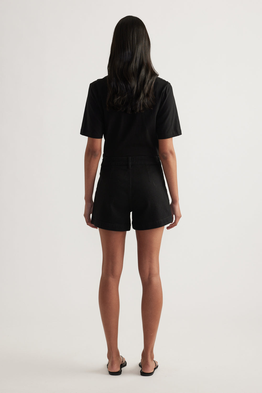 Back view of a woman wearing black high rise denim shorts with a black T shirt