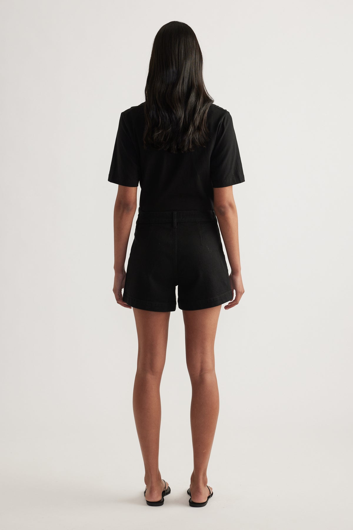 Back view of a woman wearing black high rise denim shorts with a black T shirt