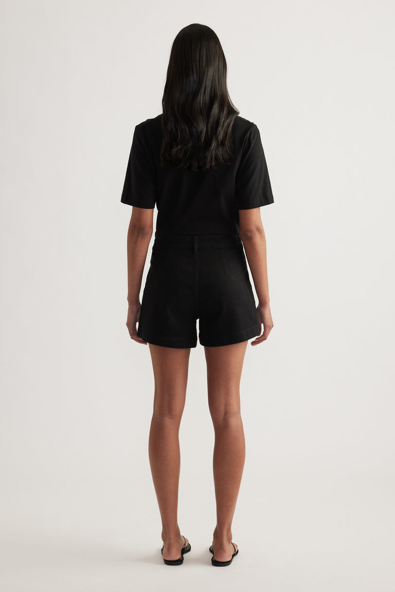 Back view of a woman wearing black high rise denim shorts with a black T shirt