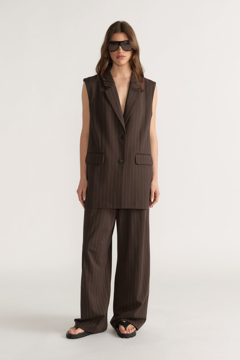 Woman wearing sleeveless dark brown pinstripe vest with matching wide-leg pants and black sandals on neutral background
