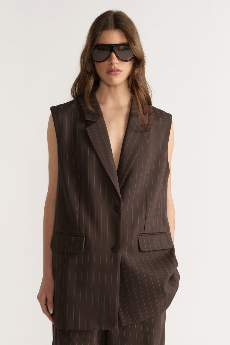 Woman wearing sleeveless dark brown pinstripe vest with padded shoulders and front pockets, styled with sunglasses