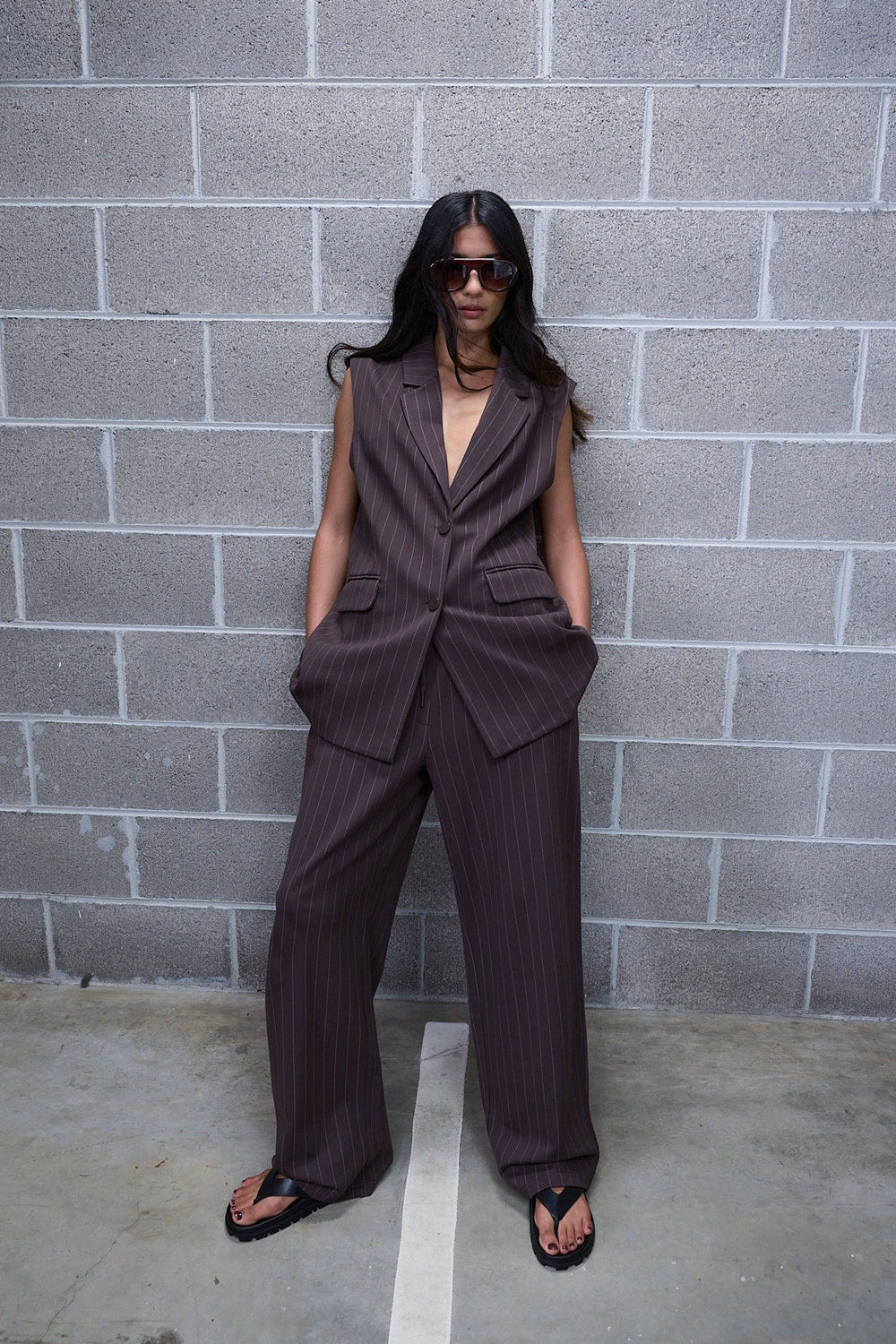 Woman wearing dark pinstripe wide leg pants with a sleeveless tailored vest and black sandals