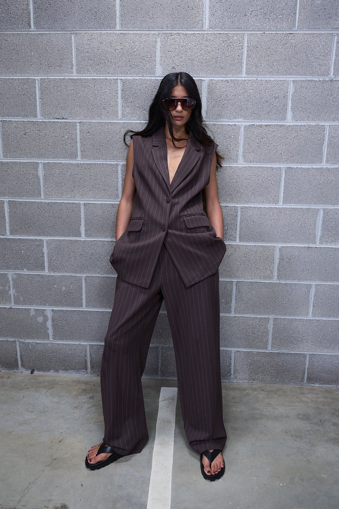 Woman wearing dark pinstripe wide leg pants with a sleeveless tailored vest and black sandals