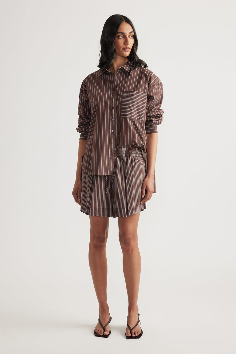 Woman wearing a brown striped oversized button through shirt with rolled sleeves and black heeled sandals