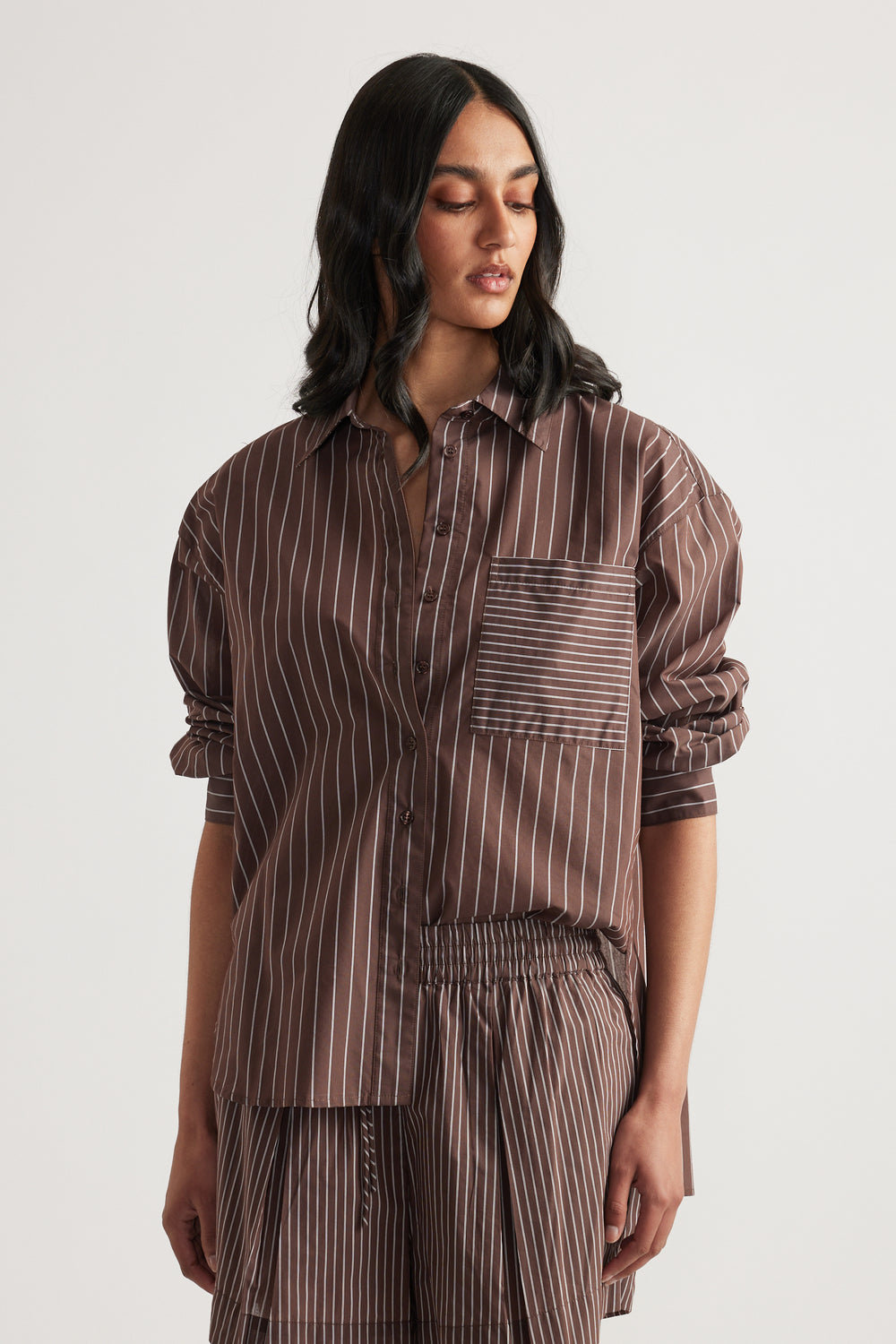Woman wearing an oversized brown striped button shirt with rolled sleeves and matching pants