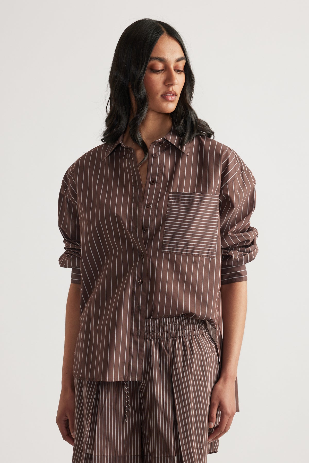 Woman wearing an oversized brown striped button shirt with rolled sleeves and matching pants