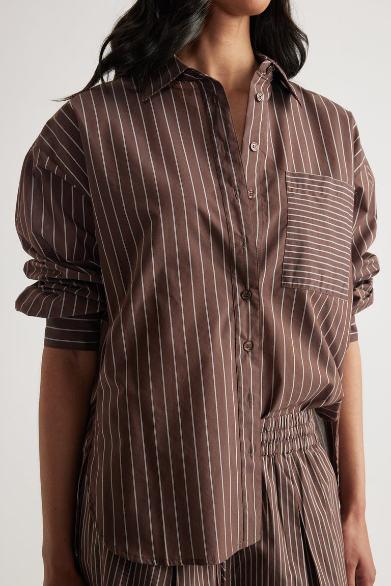 Woman wearing a brown oversized striped button-up shirt with rolled sleeves and matching pants