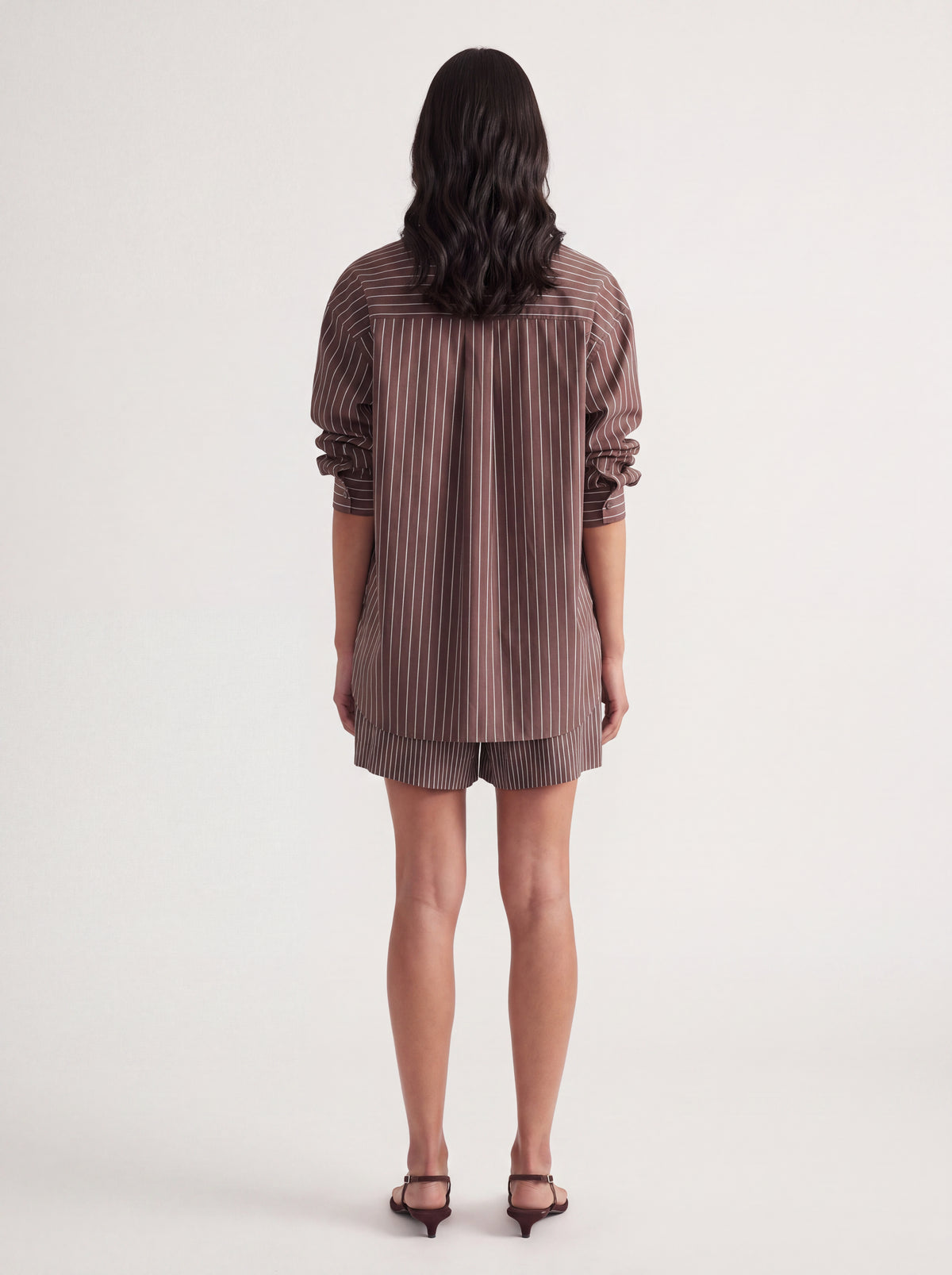 Back view of a woman wearing an oversized brown striped shirt with rolled sleeves and a curved hem