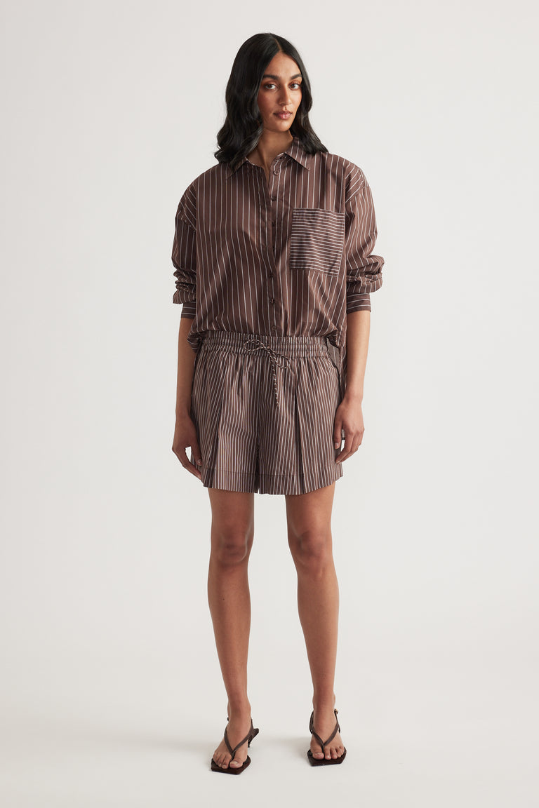 Woman wearing a brown striped button up shirt with matching pull on shorts and flat sandals
