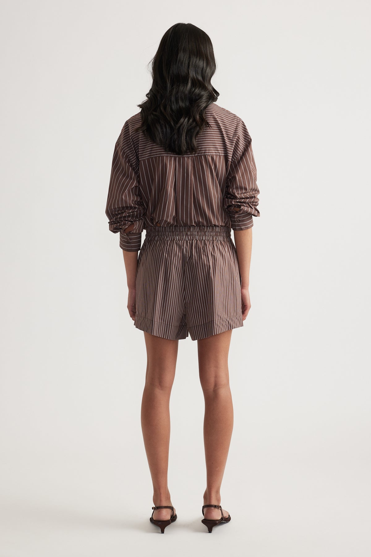Woman wearing brown striped pull-on shorts with a matching shirt and black heels