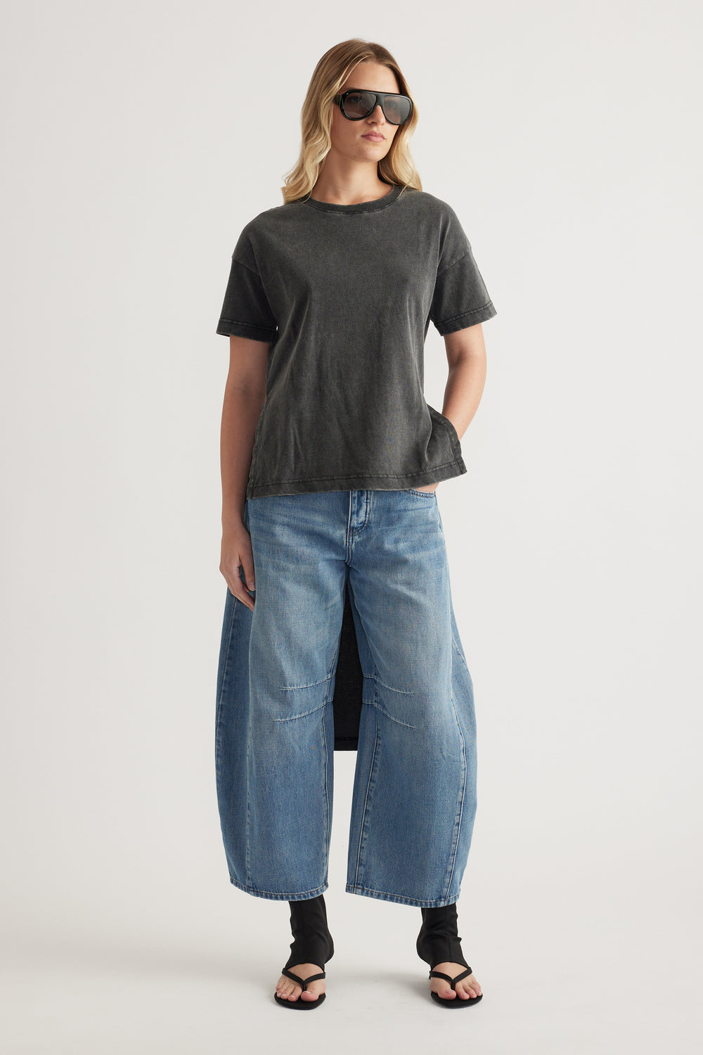 Woman wearing a charcoal high low hem tee with wide leg blue jeans and sandals