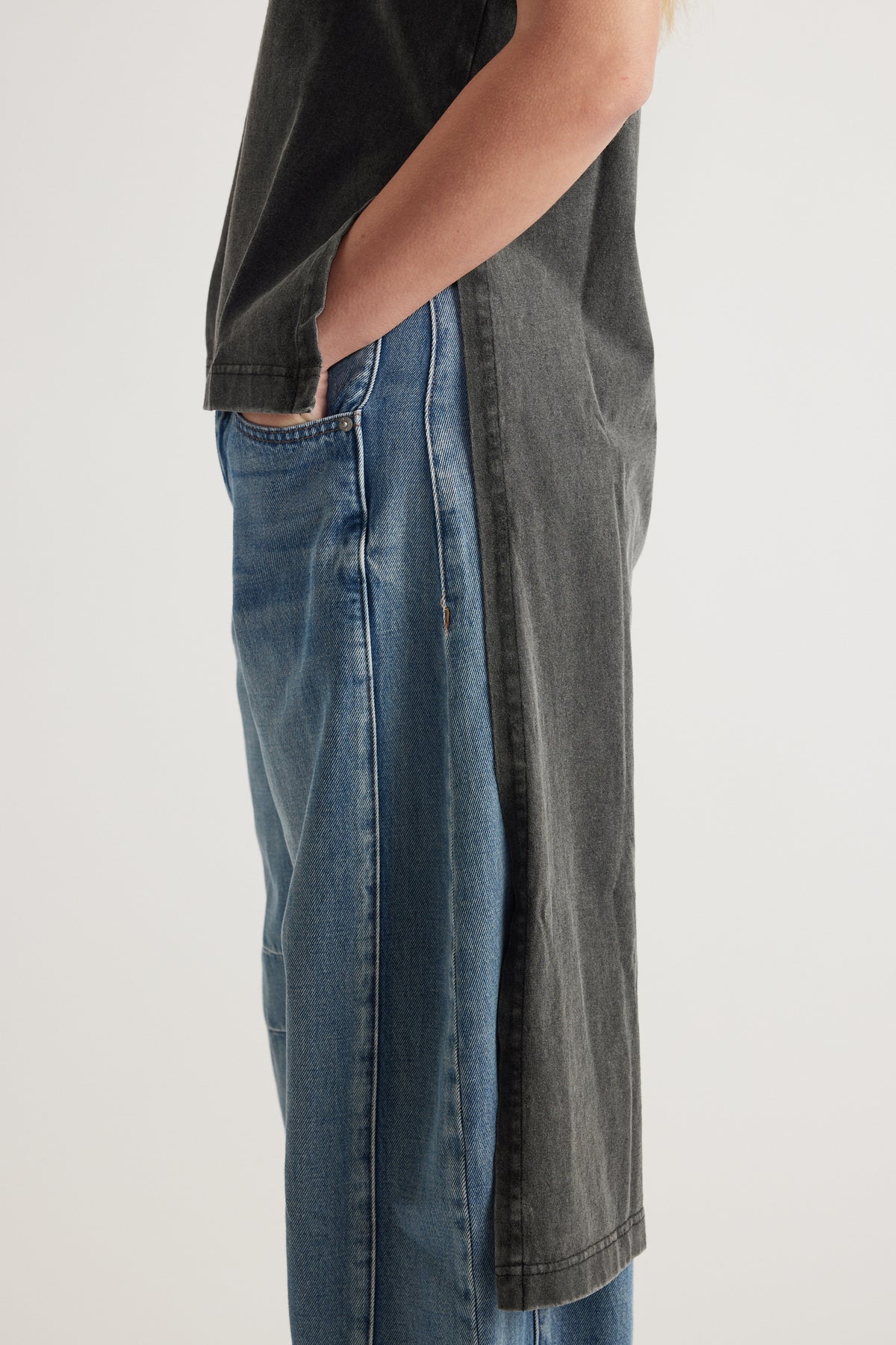 Side view of a model wearing a charcoal longline tee with a high low hem over blue jeans