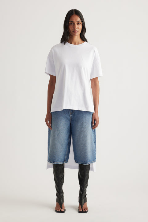 Woman wearing a white high-low hem tee with denim shorts and black knee-high boots