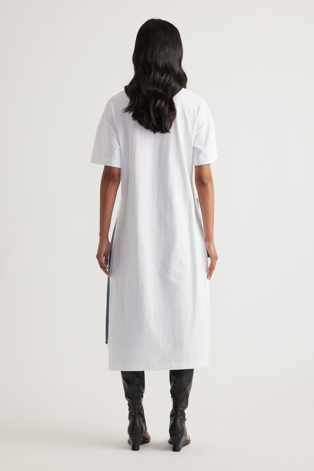 Woman wearing a white longline tee with a high low hem and black knee high boots, viewed from behind