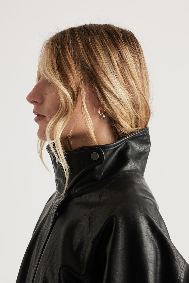 Profile of woman with wavy blonde hair wearing rhinestone pendant earrings and a high-collar black leather jacket