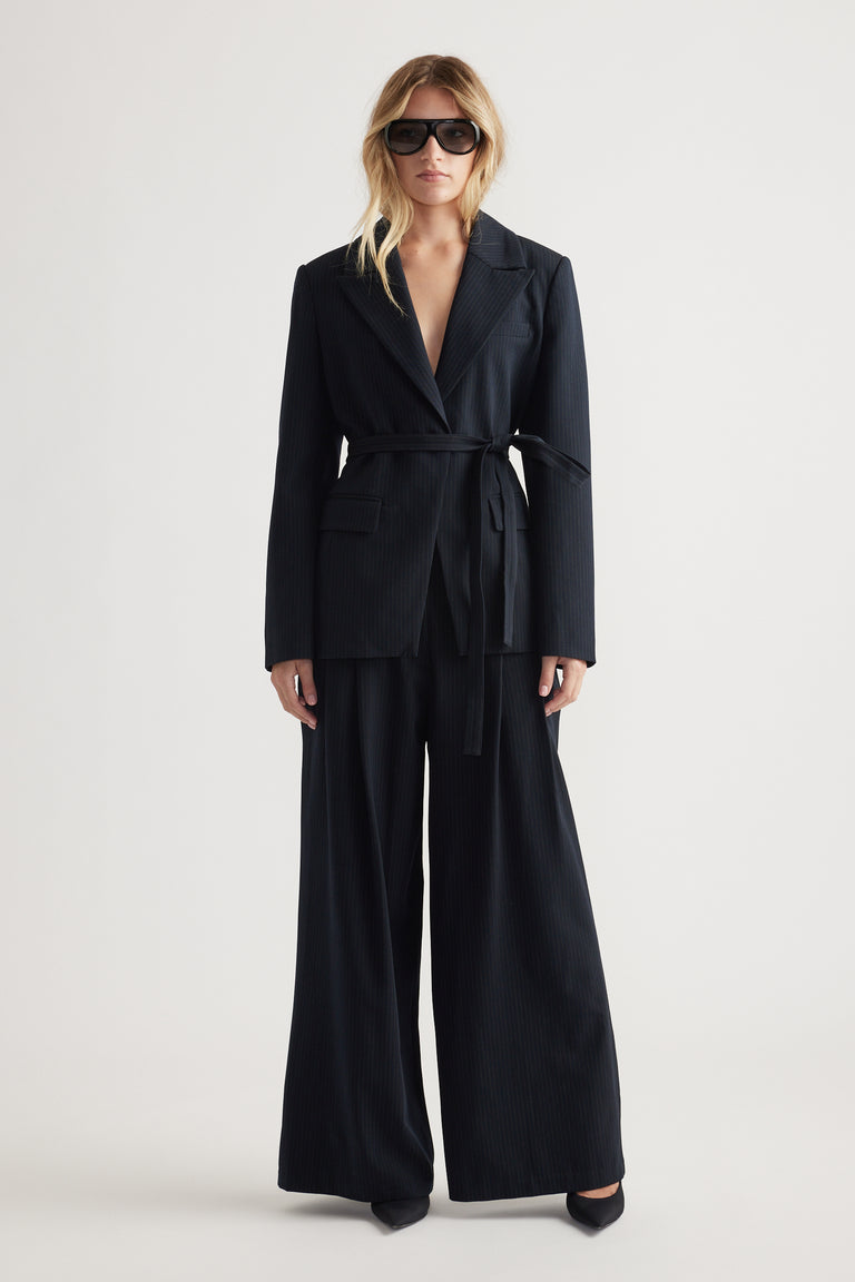 Woman wearing a navy tailored blazer with a belt, paired with wide-leg matching pants and oversized sunglasses