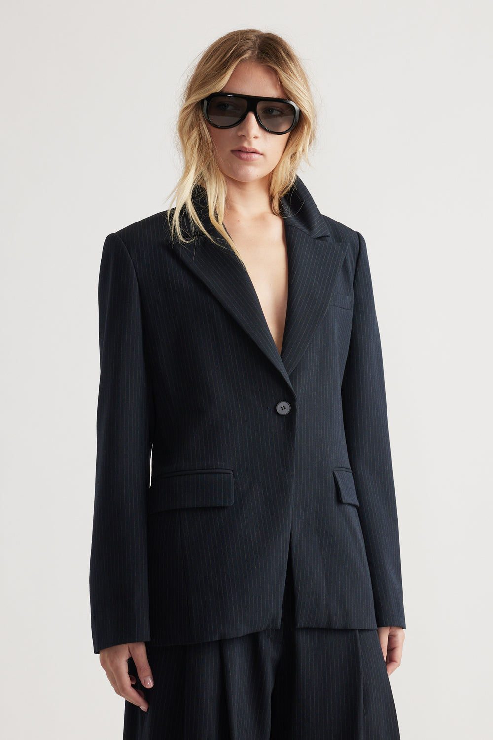 Woman wearing a navy tailored blazer with subtle pinstripes and matching wide-leg trousers in soft lighting