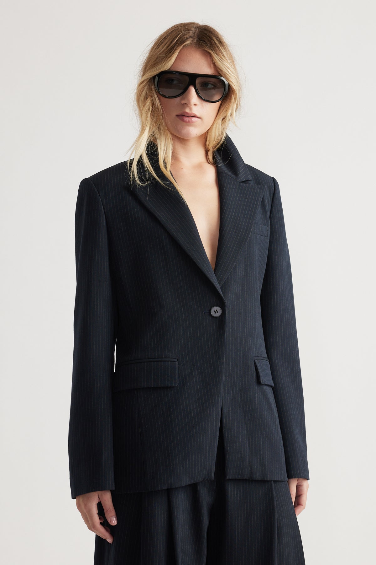 Woman wearing a navy tailored blazer with subtle pinstripes and matching wide-leg trousers in soft lighting