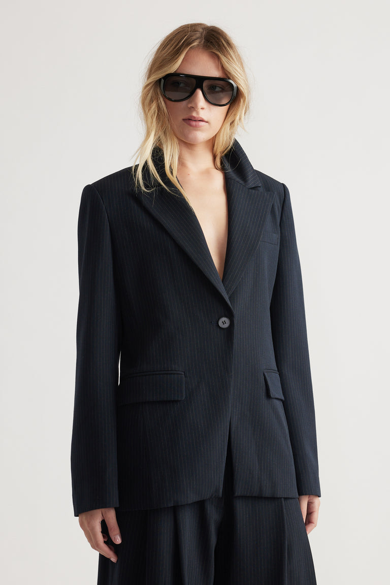 Woman wearing a navy tailored blazer with subtle pinstripes and matching wide-leg trousers in soft lighting