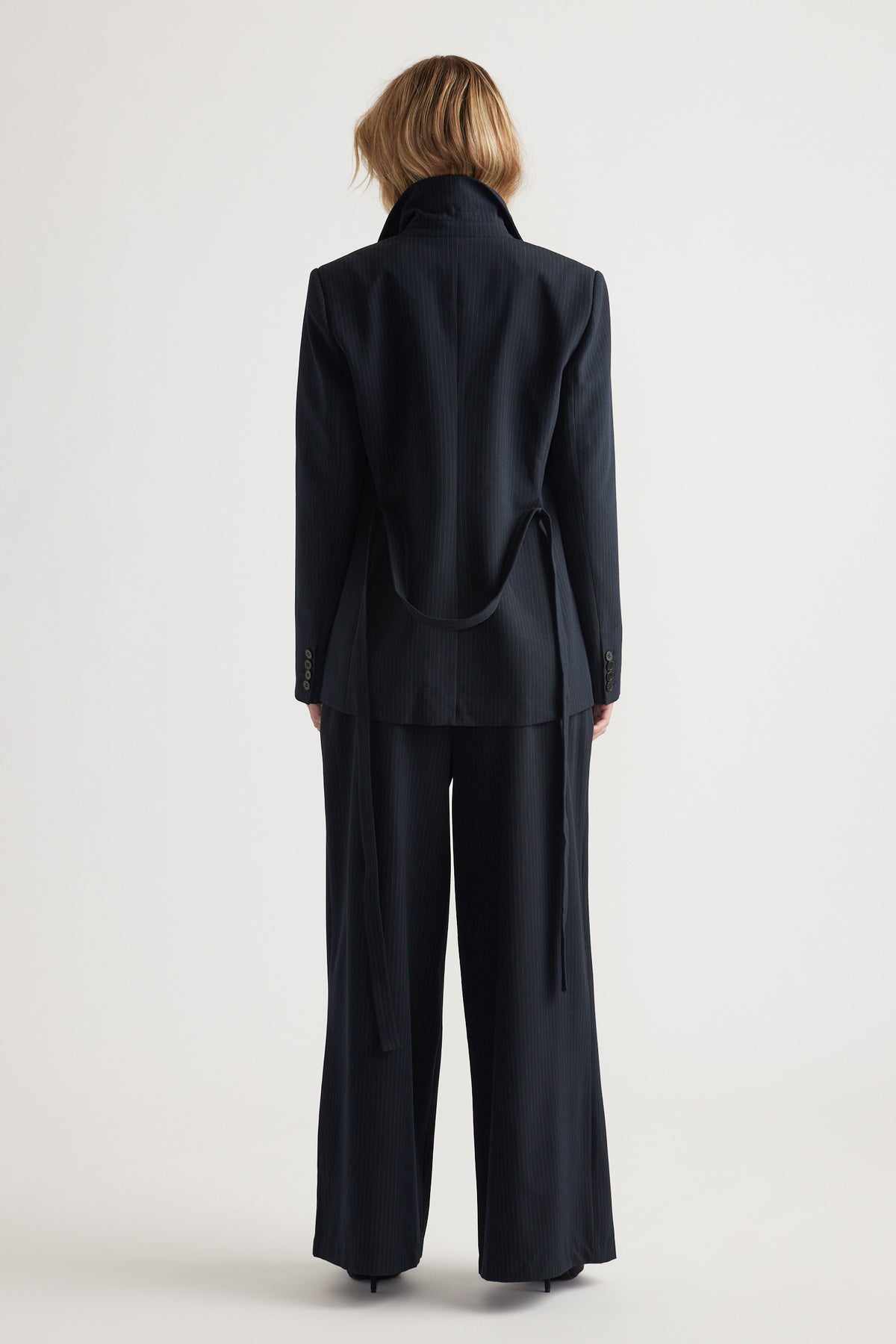 Back view of woman wearing a navy tailored blazer with matching wide-leg pants in a minimalist setting