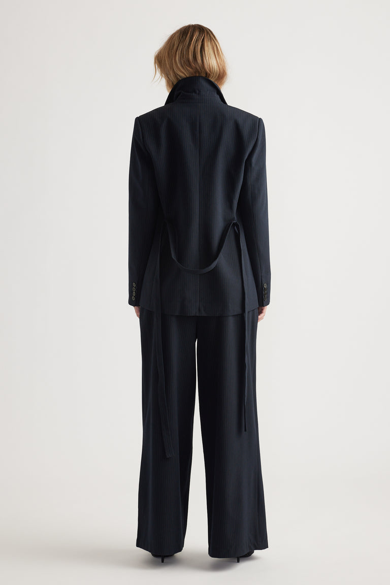 Back view of woman wearing a navy tailored blazer with matching wide-leg pants in a minimalist setting