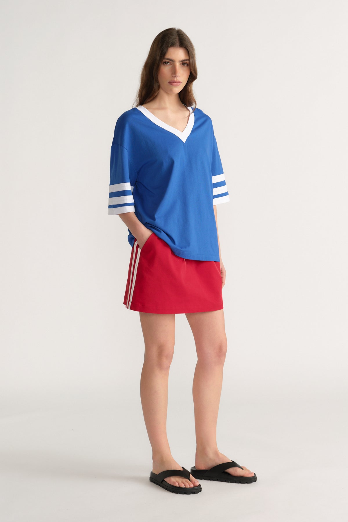 Woman styling an oversized blue V-neck tee with striped sleeves, red mini skirt and black sandals