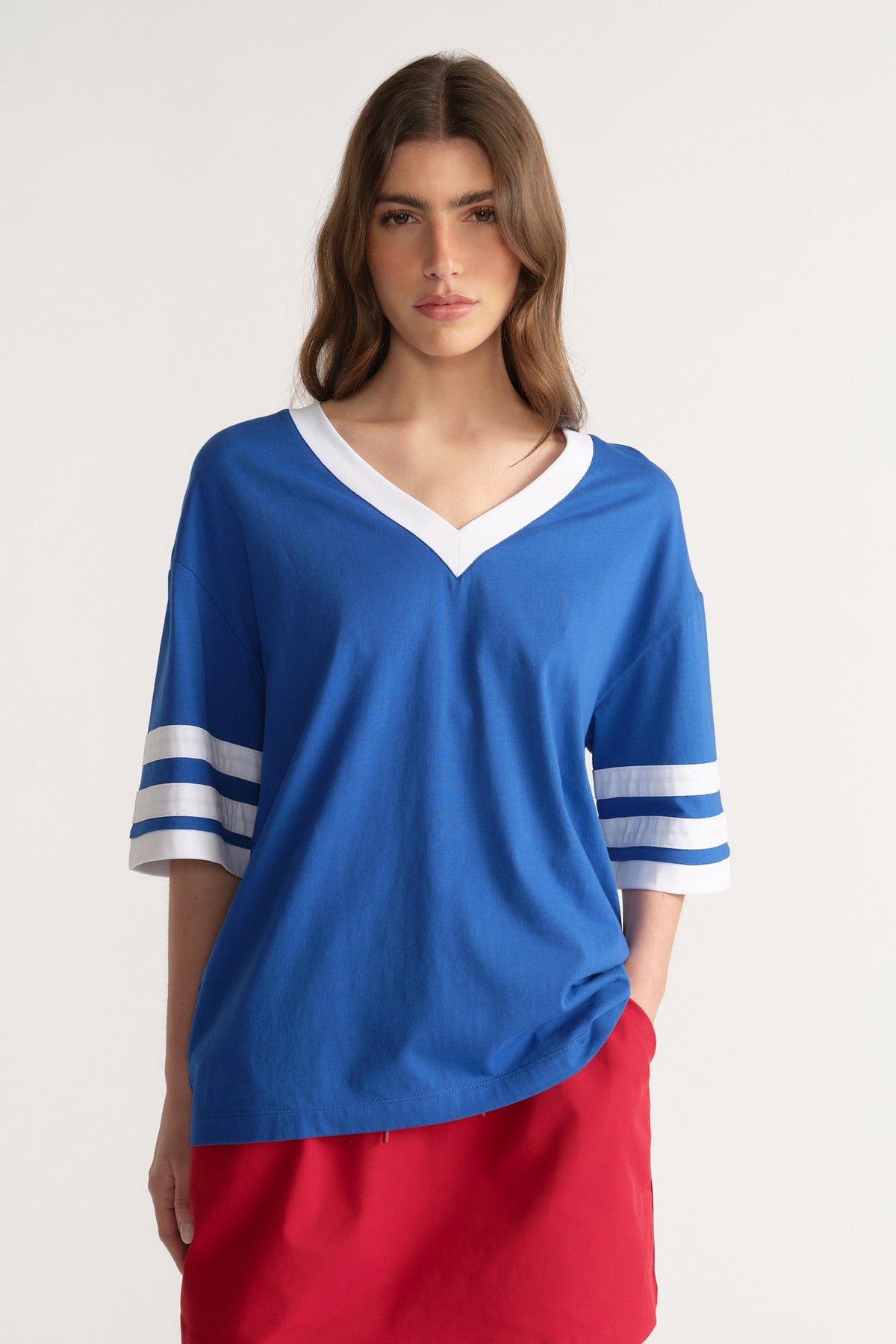 Woman wearing an oversized blue V-neck tee with white striped sleeves and a red skirt
