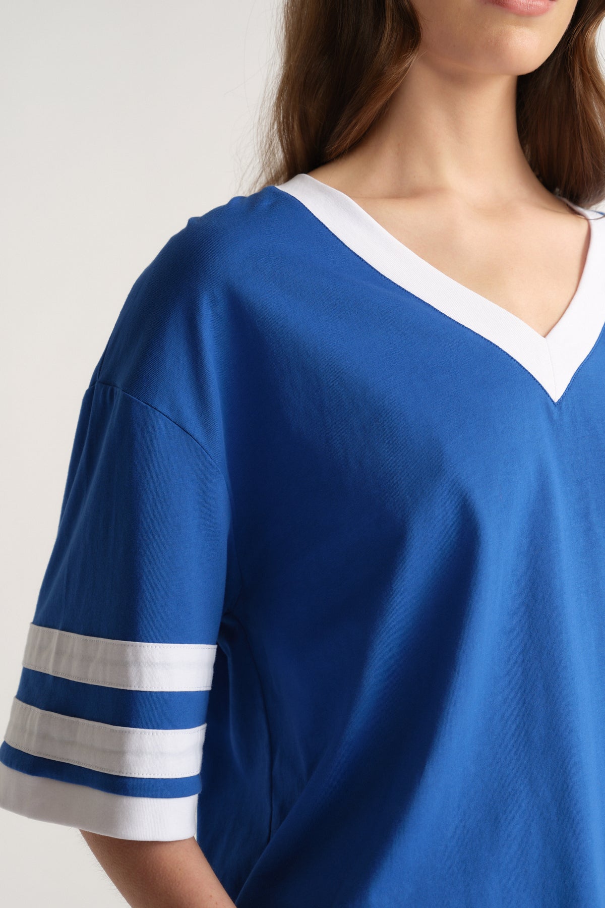 Woman wearing an oversized blue V-neck tee with white trim and striped mid-length sleeves