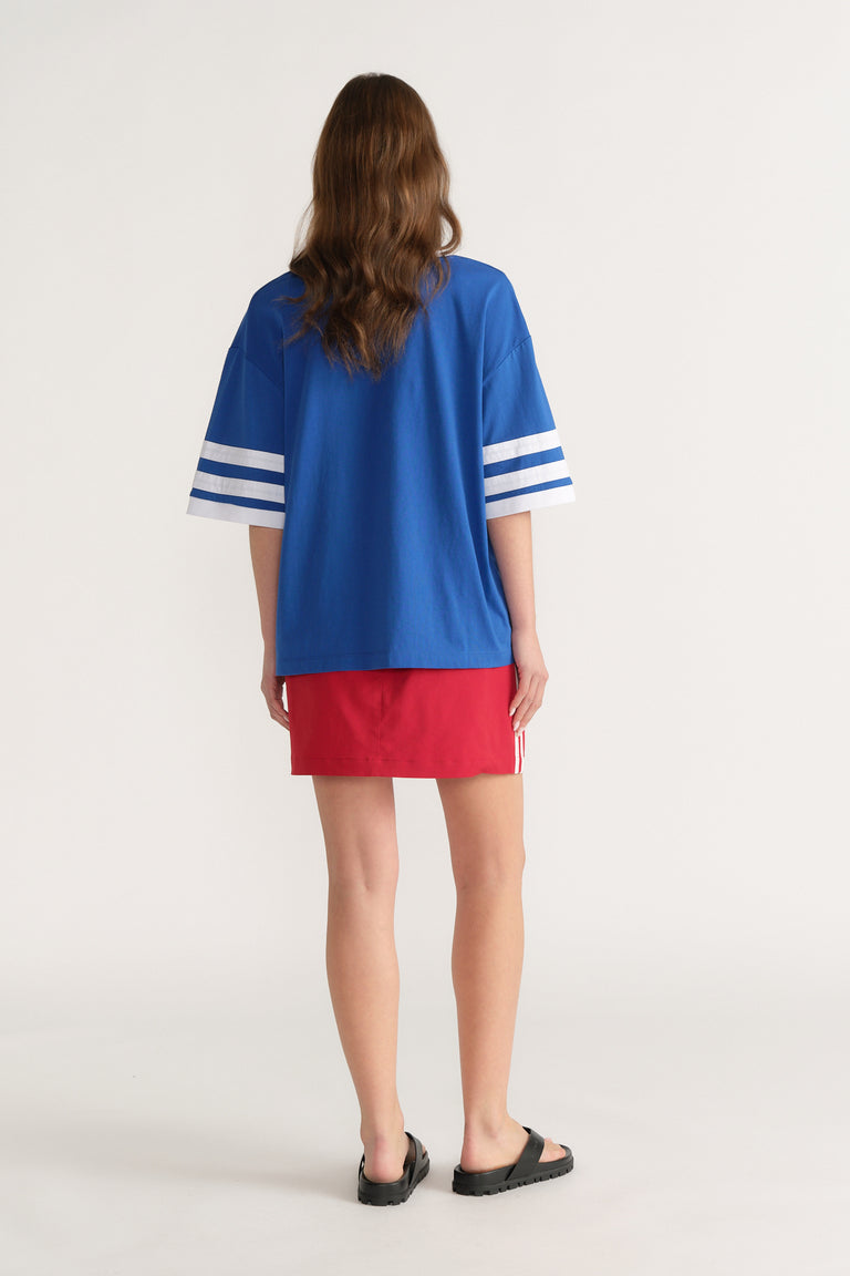 Back view of a woman wearing a cobalt blue tee with white sleeve stripes, red mini skirt and black sandals