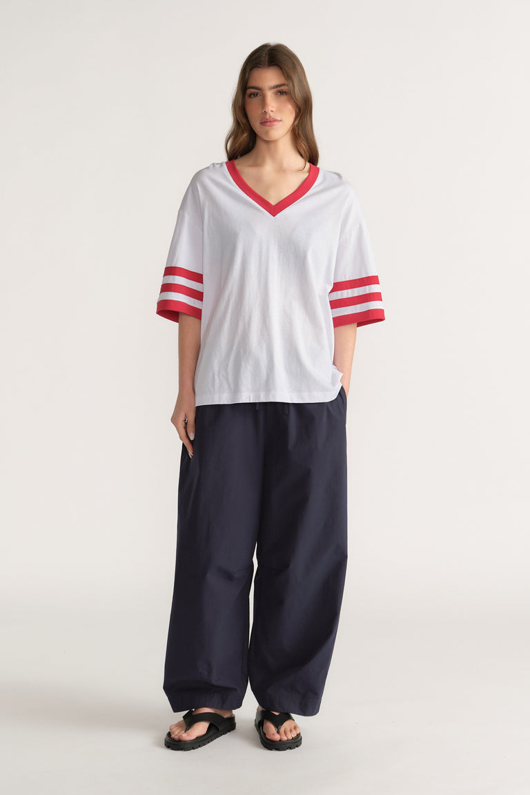 Woman wearing an oversized white V-neck tee with red stripes, navy wide-leg pants and black sandals