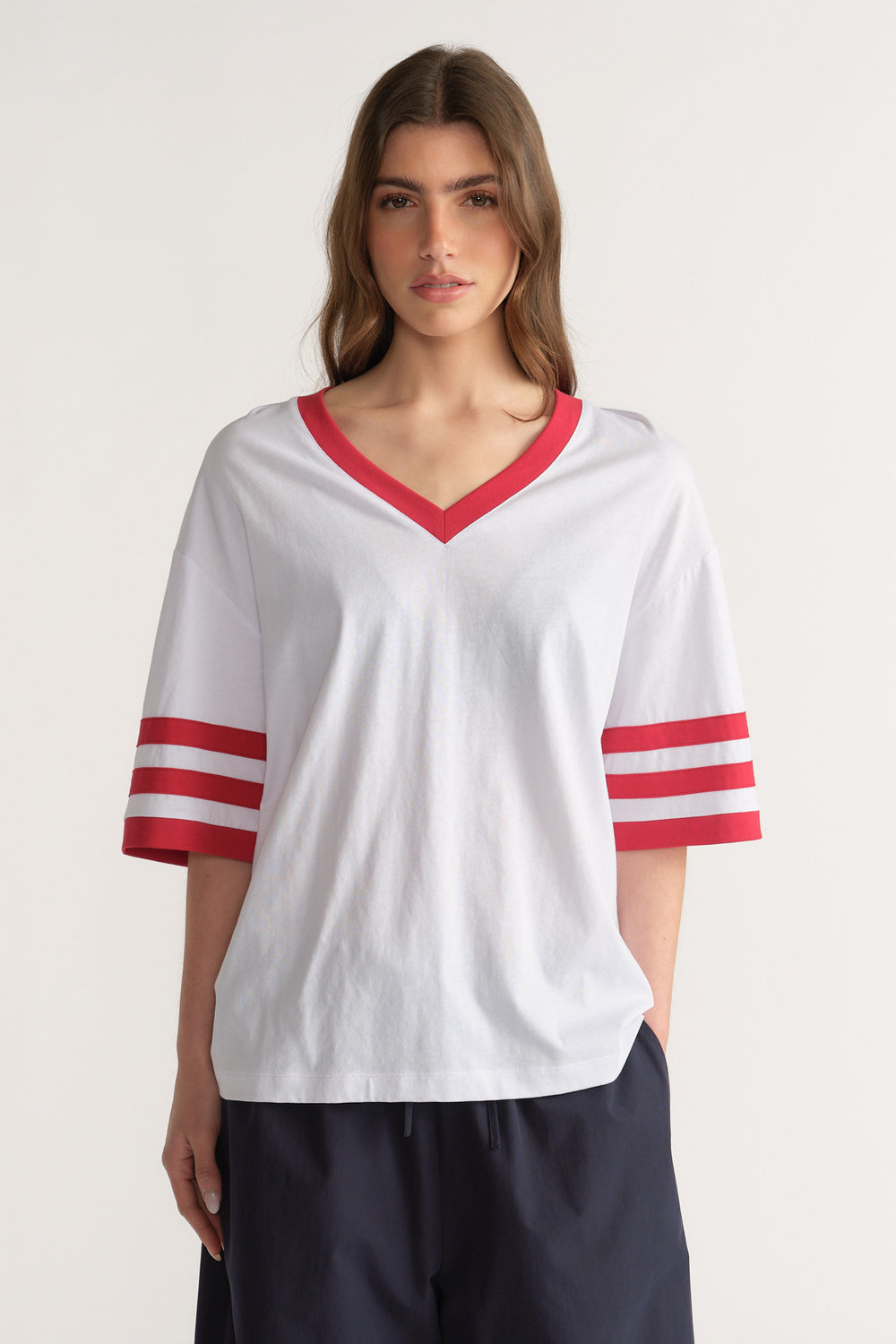 Woman in an oversized white V-neck tee with red trim and striped sleeves, paired with navy pants