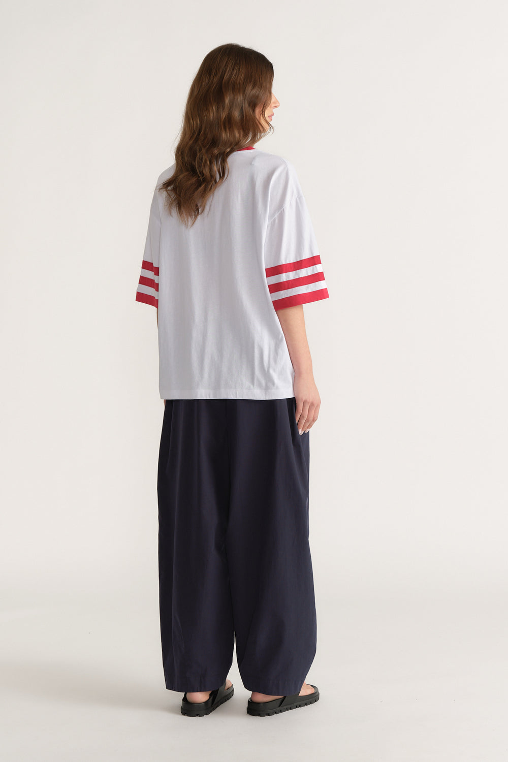 Back view of a woman wearing a white tee with red sleeve stripes, black wide leg pants and black sandals