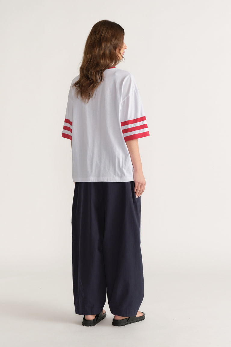 Back view of a woman wearing a white tee with red sleeve stripes, black wide leg pants and black sandals
