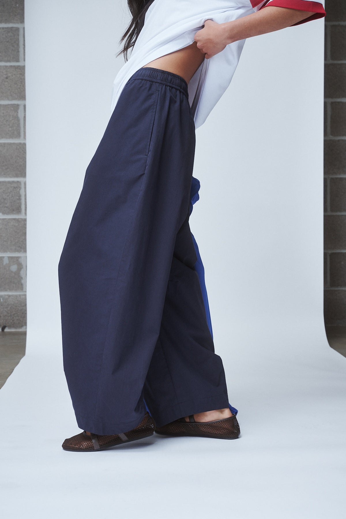 Woman wearing navy barrel leg pants with an elastic waist, a white tee and brown flats