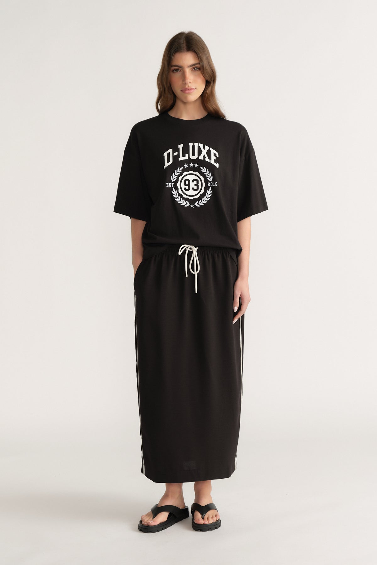 Woman wearing a black oversized D-Luxe graphic tee with a matching black maxi skirt and sandals