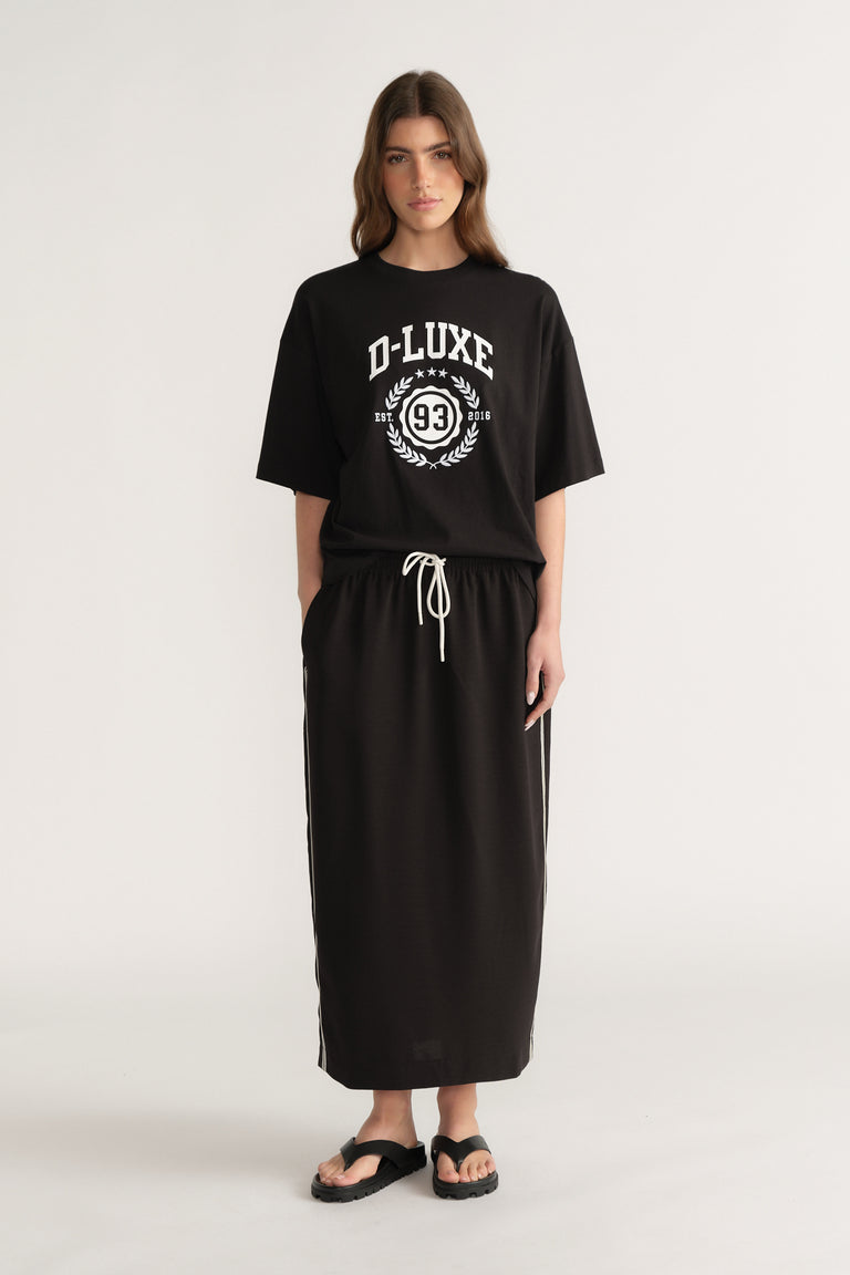 Woman wearing a black oversized D-Luxe graphic tee with a matching black maxi skirt and sandals